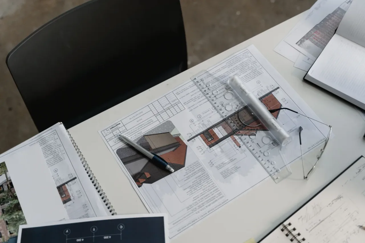 Planos técnicos de un proyecto de arquitectura de vivienda desplegados sobre una mesa de trabajo con escalímetro
